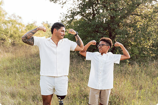 A father and son grinning as they flex their arm muscles.